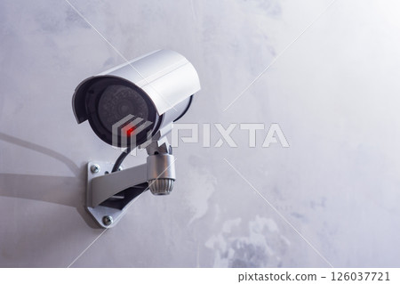 CCTV security camera with a glowing red light is mounted on a gray wall. Security and technology concept. 126037721