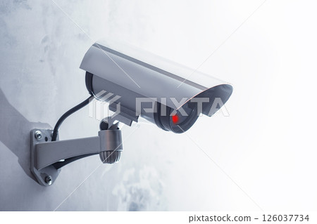 CCTV security camera with a glowing red light is mounted on a gray wall. Security and technology concept. 126037734