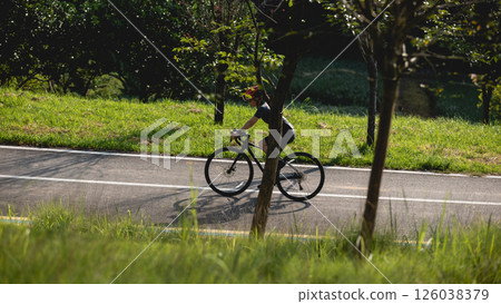 Woman cyclist morning exercise riding bike in summer park 126038379