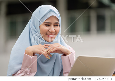 Muslim woman in hijab smiling while working on laptop for business success 126038404