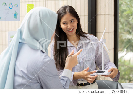 Promoting Wind Energy Awareness. Two professionals discuss sustainable energy initiatives using a wind turbine model as a focal point. Promoting Wind Energy Awareness. Two professionals discuss sustainable energy initiatives using a wind turbine model as a focal point. 126038433