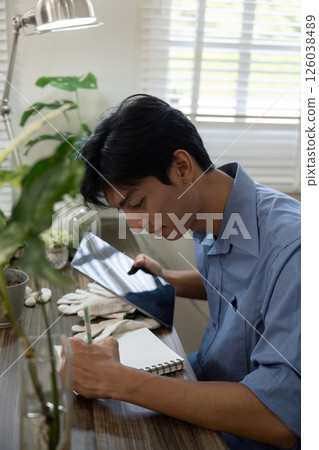 Gardening and Creativity. A young man focuses on his planting process by writing notes. 126038489