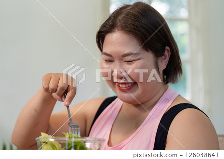 Happy overweight woman enjoying a fresh salad for healthy weight loss. 126038641