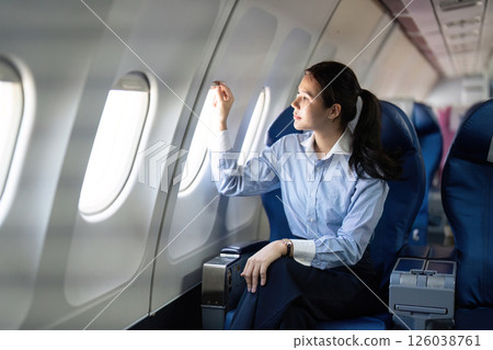 Business travel: Young woman contemplating while gazing out the airplane window Business travel: Young woman contemplating while gazing out the airplane window 126038761