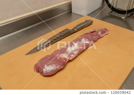 Pork tenderloin being cut on a cutting board with a stainless steel knife Pork tenderloin being cut on a cutting board with a stainless steel knife 126039042