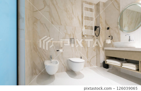 A clean modern hotel bathroom with toilet, bidet, and sink in elegant marble interior 126039065