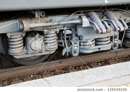Detailed view of train undercarriage showcasing suspension system and wheel assembly at a railway station Detailed view of train undercarriage showcasing suspension system and wheel assembly at a railway station 126039206