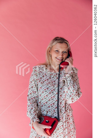 Beautiful woman in summer dress talking on vintage phone and smiling on pink background 126040362