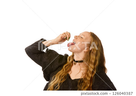 Woman in black dress tilts head back, squeezing green lime into open mouth against white studio background. Woman in black dress tilts head back, squeezing green lime into open mouth against white studio background. 126040387