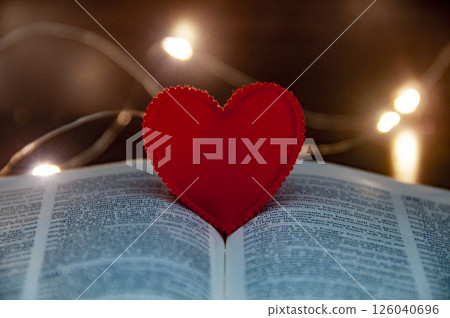 A red heart resting with the Bible reminds us of love central role in our Christian journey. A red heart resting with the Bible reminds us of love central role in our Christian journey. 126040696