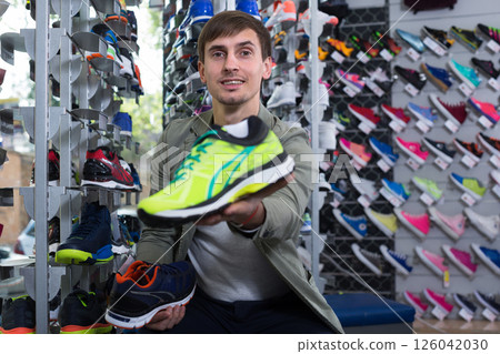 Customer proudly presenting chosen sneaker in sports store Customer proudly presenting chosen sneaker in sports store 126042030