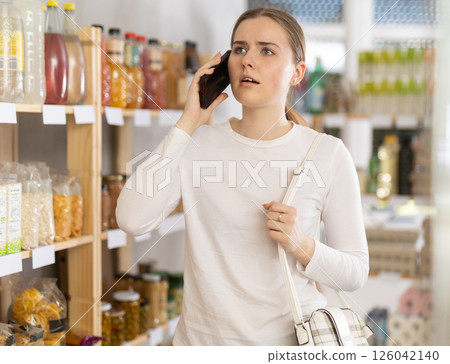 Young woman choosing groceries while talking on phone 126042140