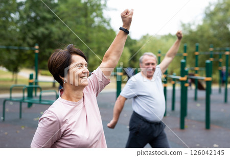 Elderly man and woman doing gymnastics on outdoor sports ground 126042145