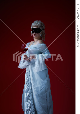 Toast of court. Noblewoman in powdered wig and dramatic dress holding glass of red wine, with bold stare on deep red background 126043724