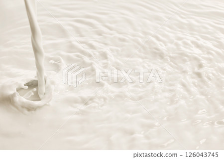 Milk pours onto milky surface forming waves and smooth textures under soft lighting. 126043745