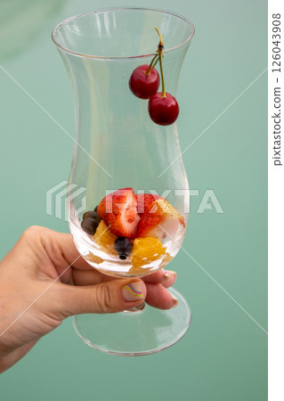 A summer cocktail with strawberries, cherries and foamy champagne in a woman's hand, against a blue pool backdrop. Party concept, vertical A summer cocktail with strawberries, cherries and foamy champagne in a woman's hand, against a blue pool backdrop. Party concept, vertical 126043908
