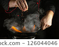 A skilled chef sprinkles aromatic spices into a hot pan filled with vibrant orange carrots, creating a burst of flavor and steam in the professional kitchen 126044046