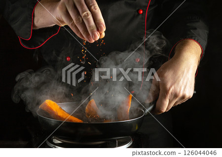 A skilled chef sprinkles aromatic spices into a hot pan filled with vibrant orange carrots, creating a burst of flavor and steam in the professional kitchen A skilled chef sprinkles aromatic spices into a hot pan filled with vibrant orange carrots, creating a burst of flavor and steam in the professional kitchen 126044046