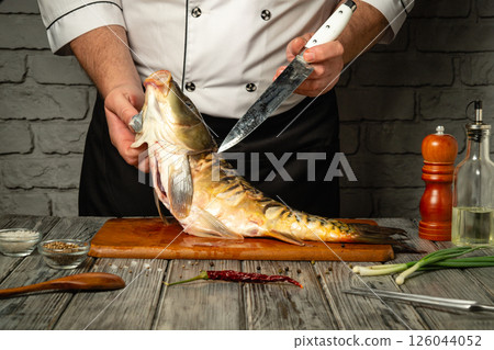 A skilled chef expertly fillets a freshly caught fish on a wooden cutting board. Various ingredients and kitchen tools are arranged nearby, enhancing the culinary atmosphere A skilled chef expertly fillets a freshly caught fish on a wooden cutting board. Various ingredients and kitchen tools are arranged nearby, enhancing the culinary atmosphere 126044052
