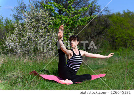 Woman practicing seated extended leg pose outdoors in spring garden. 126045121