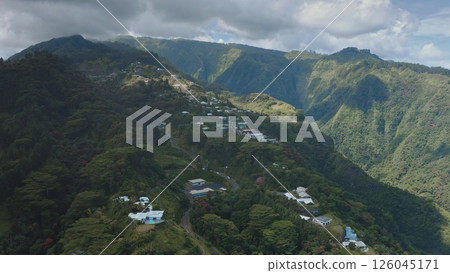 Tahiti island volcanic mountain landscape. Beautiful hills covered rainforest, lush green valleys, scattered houses village buildings under cloudy sky, showcasing French Polynesia beauty. Aerial shot Tahiti island volcanic mountain landscape. Beautiful hills covered rainforest, lush green valleys, scattered houses village buildings under cloudy sky, showcasing French Polynesia beauty. Aerial shot 126045171