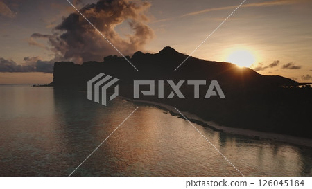 Sunset warm light over silhouette of mountain reflecting on calm ocean water surface, tropical island in French Polynesia. Beautiful landscape of untouched nature. Travel, tourism. Aerial drone flight 126045184