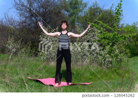 Woman practicing yoga standing outdoors in spring garden. Woman practicing yoga standing outdoors in spring garden. 126045262