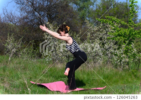 Woman balancing in yoga pose outdoors on pink mat. Woman balancing in yoga pose outdoors on pink mat. 126045263