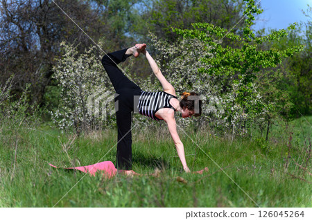 Woman practicing balancing yoga pose outdoors in spring field. 126045264