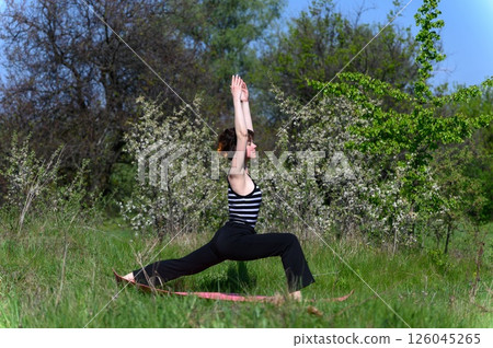 Woman practicing warrior one pose outdoors in spring garden. Woman practicing warrior one pose outdoors in spring garden. 126045265