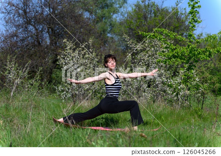 Woman practicing warrior two pose outdoors in spring garden. Woman practicing warrior two pose outdoors in spring garden. 126045266