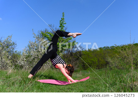 Woman practicing three-legged downward dog pose outdoors in spring garden. Woman practicing three-legged downward dog pose outdoors in spring garden. 126045273