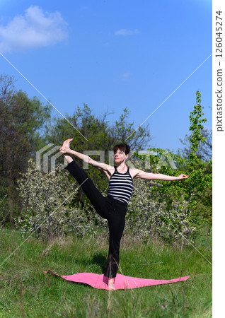 Woman practicing extended hand to big toe pose outdoors in spring garden. Woman practicing extended hand to big toe pose outdoors in spring garden. 126045274