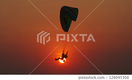Motor paraglider flying through colorful sunset sky 126045308
