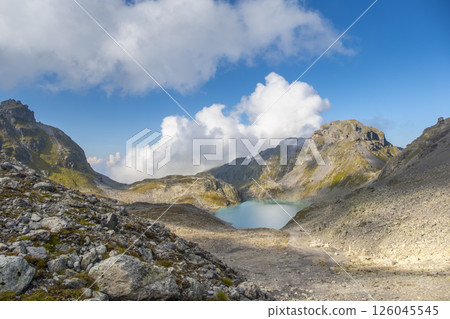 Captivating landscape of Pizol Wildsee lake in the Swiss Alps, featuring tranquil turquoise water amid rugged peaks enveloped by mist and clouds, creating a dramatic mountain scene 126045545