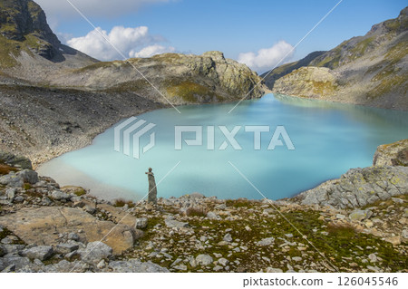 Turquoise alpine lake surrounded by rocky mountain peaks and grass-covered slopes under a partly cloudy sky in the Pizol region. The natural beauty of the serene landscape is highlighted Turquoise alpine lake surrounded by rocky mountain peaks and grass-covered slopes under a partly cloudy sky in the Pizol region. The natural beauty of the serene landscape is highlighted 126045546