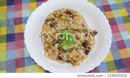 close up of homemade egg fried rice with charr siu port, eggs, shrimps and coriander as toppings in a white plate on a colourful table cloth  126045638
