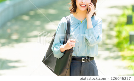 Smiling woman/businesswoman talking on her smartphone while walking along the promenade Smiling woman/businesswoman talking on her smartphone while walking along the promenade 126046257