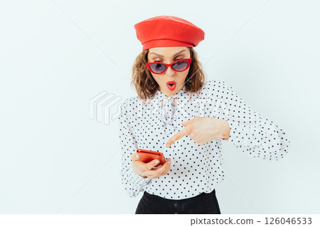 A woman in a red hat and sunglasses pointing at a cell phone 126046533