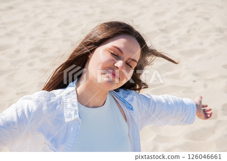 Young caucasian woman enjoying sun on sandy beach with open arms and eyes closed, embracing relaxation and freedom. Digital nomad lifestyle. Remote work Young caucasian woman enjoying sun on sandy beach with open arms and eyes closed, embracing relaxation and freedom. Digital nomad lifestyle. Remote work 126046661