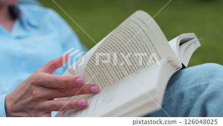 Close up of hands woman reading book in the yard in summer. Close up of hands woman reading book in the yard in summer. 126048025
