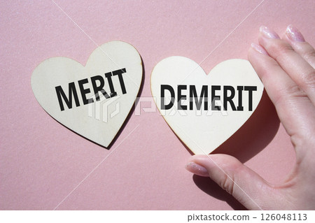 Merit or Demerit symbol. Concept word Merit or Demerit on wooden hearts. Businessman hand. Beautiful pink background. Business and Merit or Demerit concept. Copy space 126048113