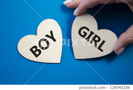 Boy or Girl symbol. Concept word Boy or Girl on wooden hearts. Man hand. Beautiful blue background. Gender and Boy or Girl concept. Copy space 126048286