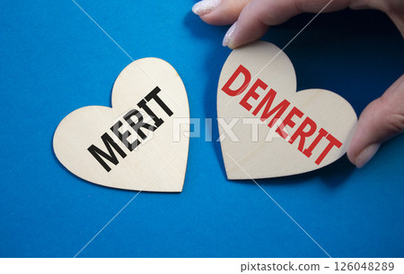 Merit or Demerit symbol. Concept word Merit or Demerit on wooden hearts. Businessman hand. Beautiful blue background. Business and Merit or Demerit concept. Copy space Merit or Demerit symbol. Concept word Merit or Demerit on wooden hearts. Businessman hand. Beautiful blue background. Business and Merit or Demerit concept. Copy space 126048289