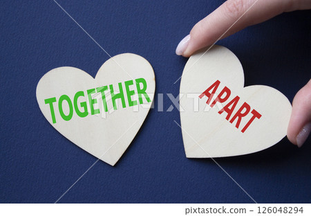 Together or Apart symbol. Concept word Together or Apart on wooden hearts. Businessman hand. Beautiful deep blue background. Business and Together or Apart concept. Copy space Together or Apart symbol. Concept word Together or Apart on wooden hearts. Businessman hand. Beautiful deep blue background. Business and Together or Apart concept. Copy space 126048294