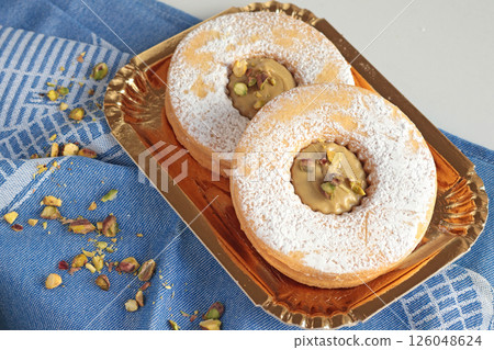 Shortbread dough biscuits with pistachio cream and nuts on gold paper plate. Dessert for party, celebration. Shortbread dough biscuits with pistachio cream and nuts on gold paper plate. Dessert for party, celebration. 126048624