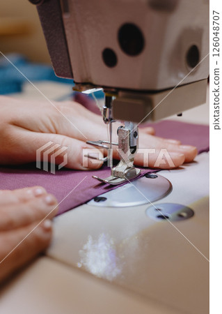 woman sews piece of cloth on sewing machine. industrial metal machine for all fabric tops.  126048707