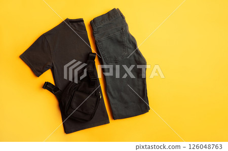 Stylish dark gray children's T-shirt with jeans and black bag. Fashion kids outfit for summer, autumn. Total grey look on yellow background. Flat lay, top view Stylish dark gray children's T-shirt with jeans and black bag. Fashion kids outfit for summer, autumn. Total grey look on yellow background. Flat lay, top view 126048763