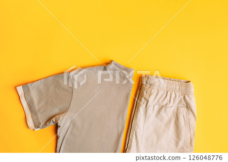Set of light gray children's clothes T-shirt with trousers. Fashion kids outfit for summer and spring. Total grey look on yellow background. Flat lay, top view 126048776