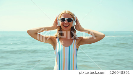 Summer portrait happy young woman smiles enjoys listening to music with headphones on beach at sea 126048891